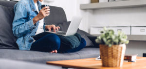 A woman types on their laptop while sitting on a couch. This could represent the comfort of online therapy in Michigan. Learn more from an online therapist in Michigan about online trauma therapy in Kent County, MI and more. 