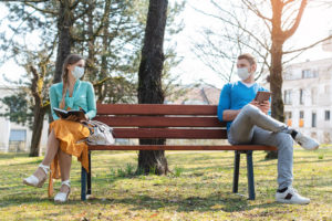 A man and woman sit on opposite sites of a park bench while wearing masks. This could represent the anxiety an anxiety therapist in Grand Rapids, MI can address. Learn more about anxiety treatment in Grand Rapids, MI and more by contacting an online anxiety therapist in Grand Rapids, MI today. 
