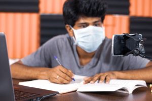 Image of teen wearing a mask and writing on a notepad. If you're looking to support your teen in Michigan, teenage counseling in Kent County, MI could be just for them! 